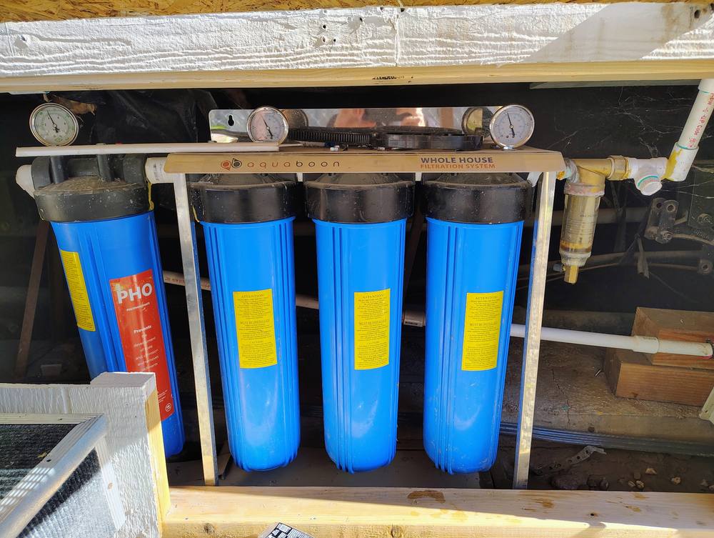 Four-stage whole house filtration system with pressure gauges and a polyphosphate scale filter.